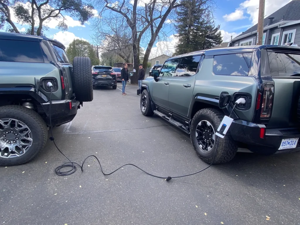 Two GMC Hummer EVs connected by a charging cable, demonstrating V2V (Vehicle-to-Vehicle) power sharing.