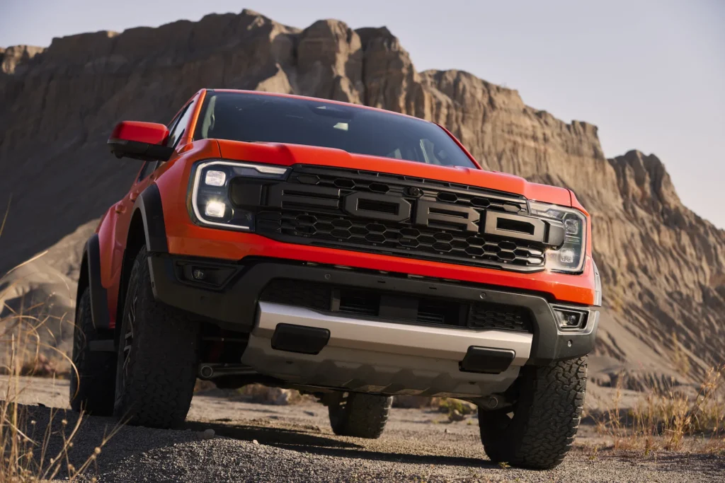 Ford Ranger Raptor Hidden Costs Front-angle exterior shot of a red Next-Gen Ford Ranger Raptor navigating rugged desert terrain, highlighting its aggressive performance-focused design and off-road capability.