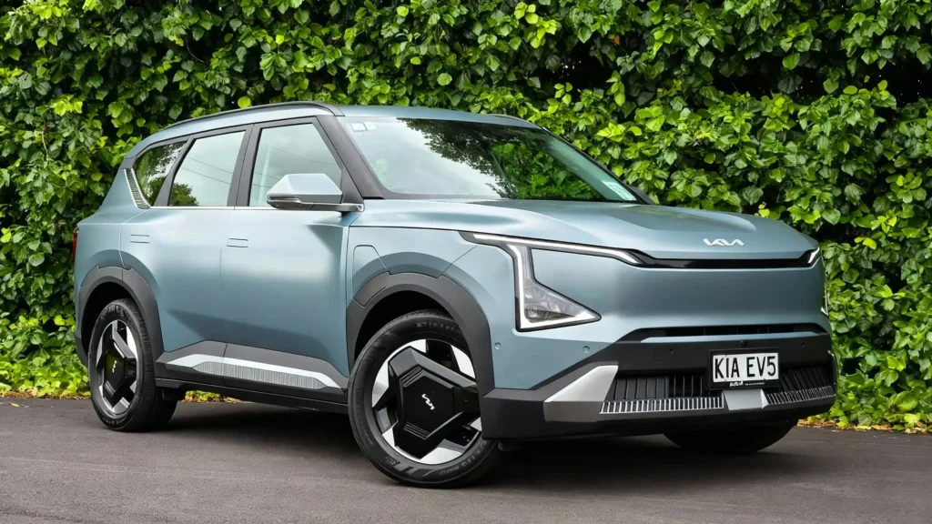 Kia EV5 global price review Real-world view of a light blue Kia EV5 parked outside against a green ivy wall, questioning its value proposition.